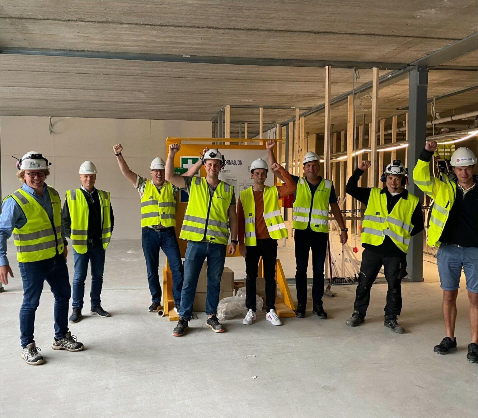 En gruppe i gule vester og hvite hjelmer inne i den nye hallen under byggingen