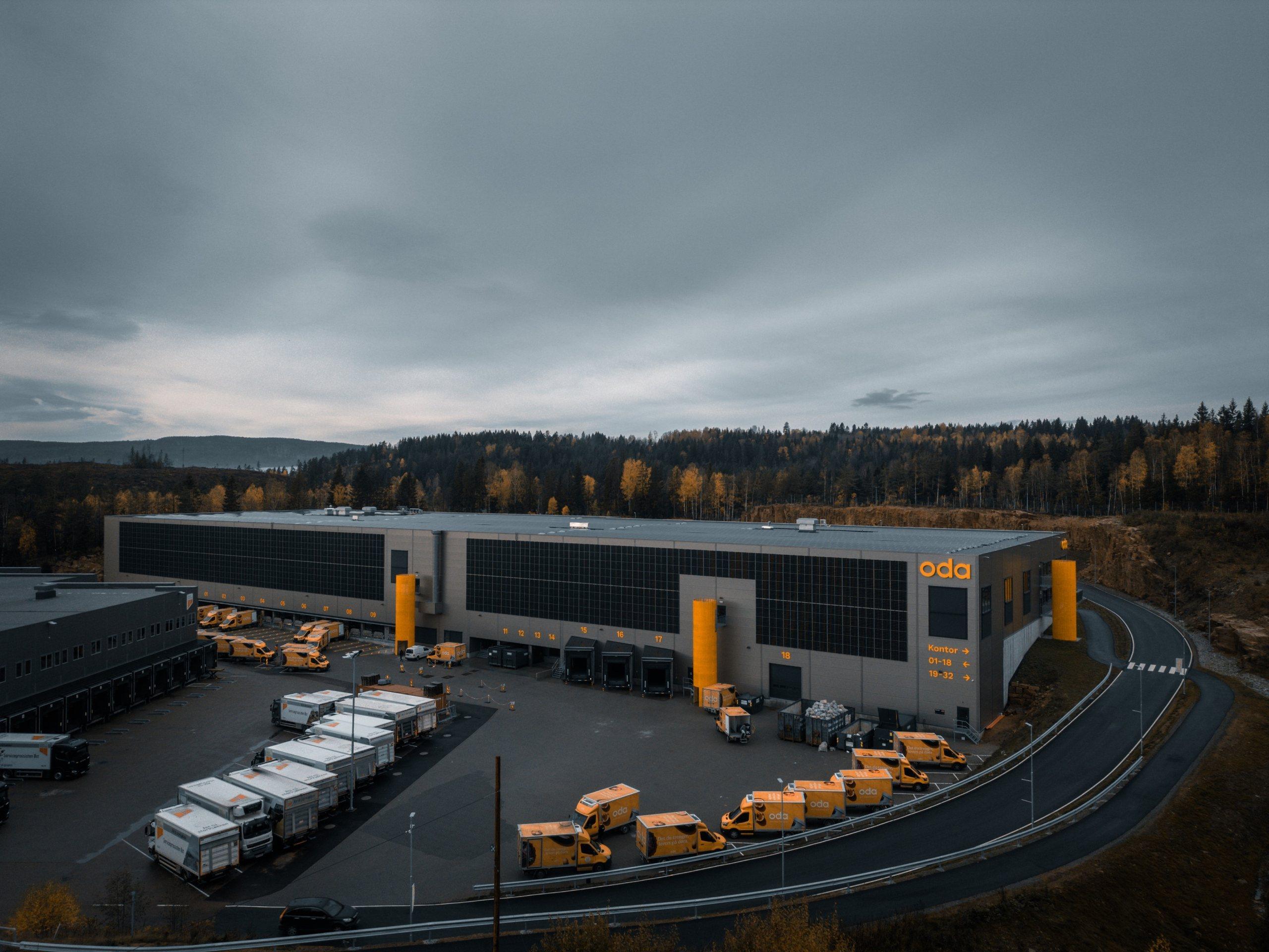 Liertoppen Vest i kveldslys: et stort, lavt lager- og produksjonsbygg med varebiler på plassen foran